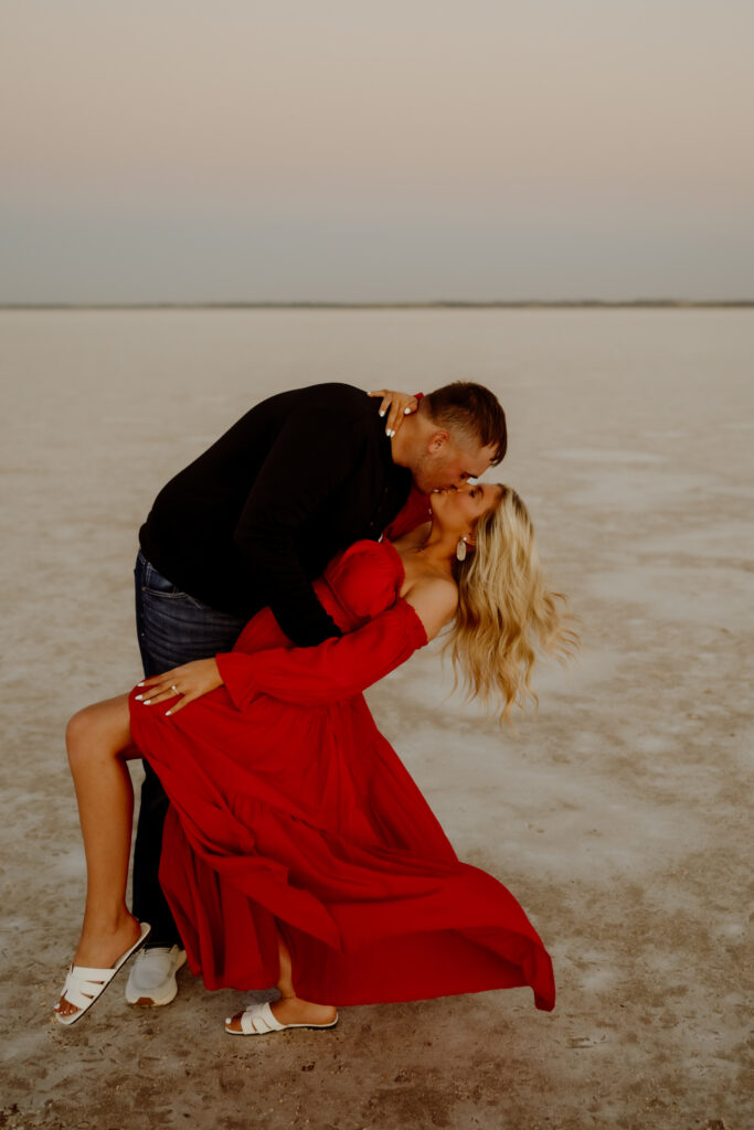 Engaged couple kissing on the wide-open salt flats of Oklahoma at sunset