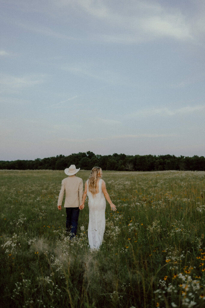 bride and groom walk through field of flowers at oklahoma rustic wedding venue