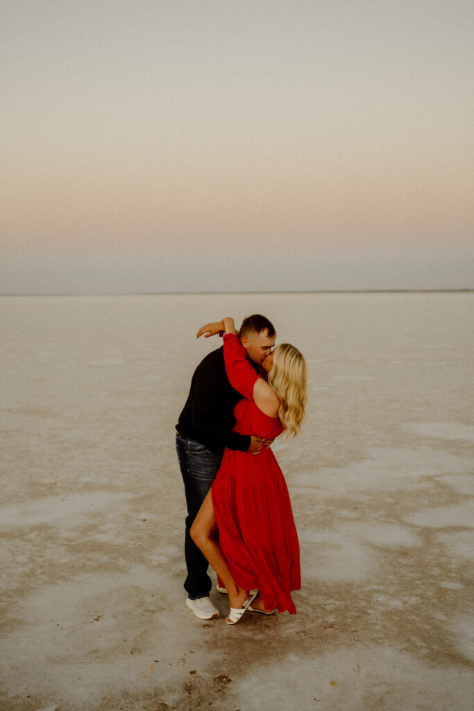 Couple embracing on the salt flats, with golden light and wide-open skies in the background