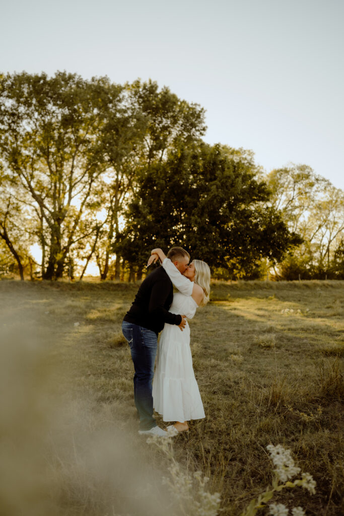 Western couple standing in an open Oklahoma field at sunset, sharing a quiet moment