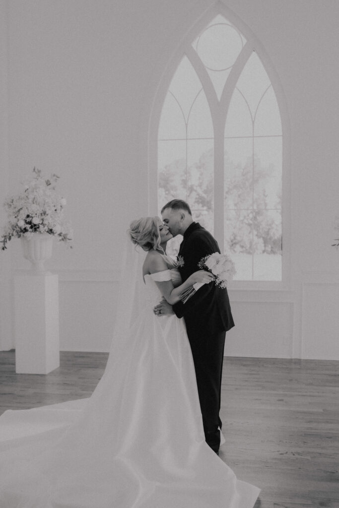 groom kisses bride on cheek inside white chapel at the springs wedding venue