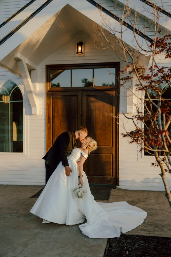 bride and groom dip kiss in front of chapel at the springs venue
