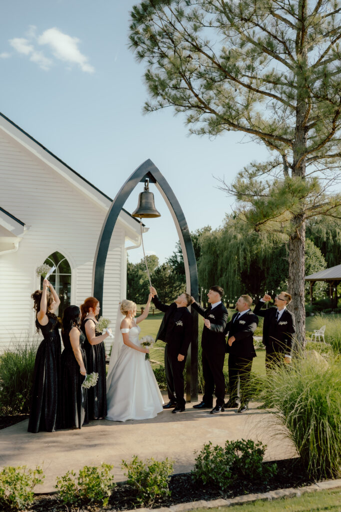 bride and groom ring wedding bell while wedding party cheers